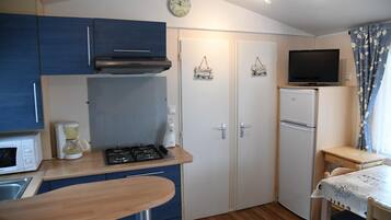 A compact kitchen with a stove, microwave, and coffee maker. There is a small refrigerator, a TV, and a table with a chair.