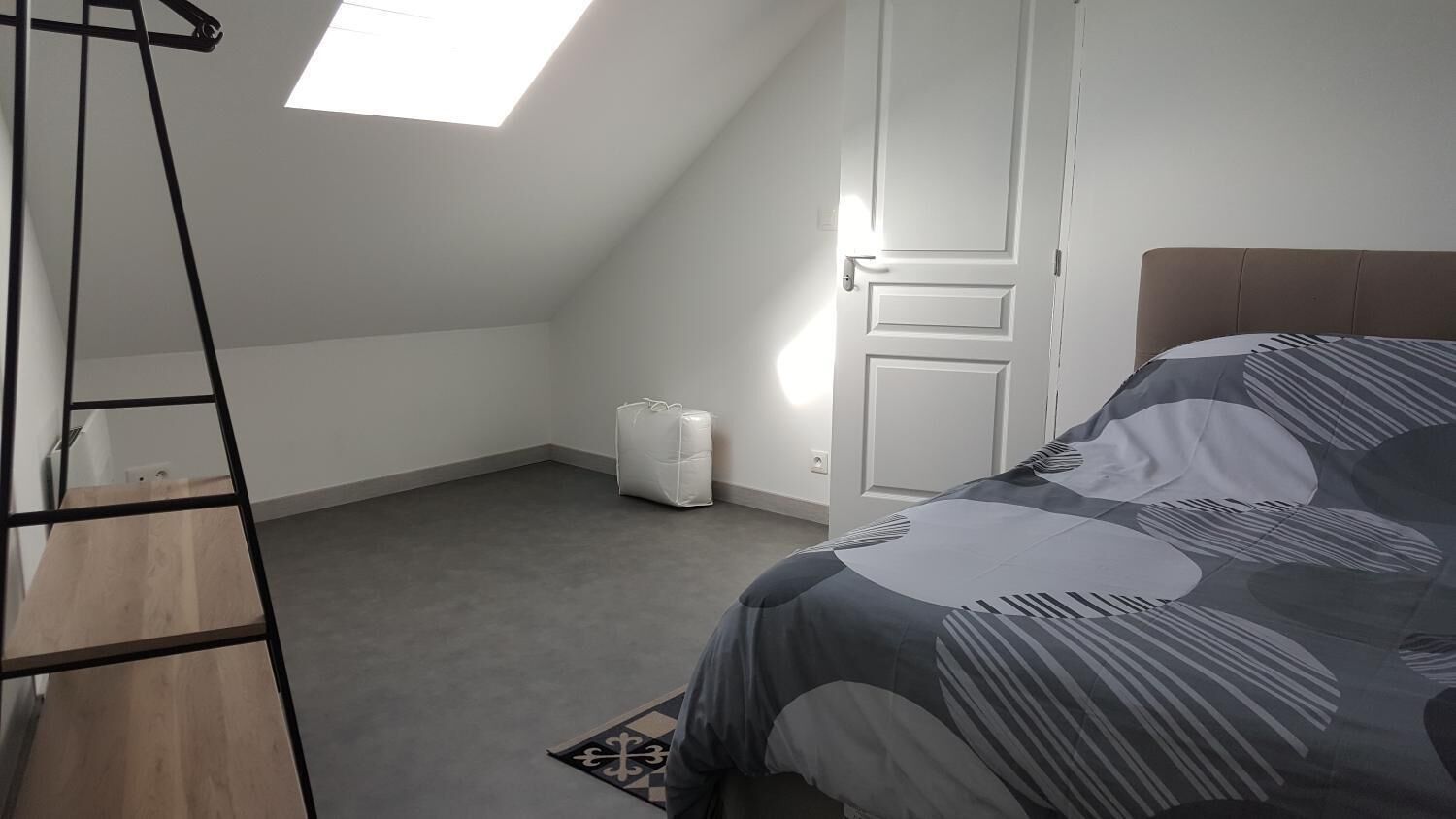 Une chambre avec un plafond en pente, un lit recouvert d’une courtepointe à motifs, une échelle et une porte blanche.