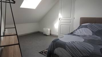 Une chambre avec un plafond en pente, un lit recouvert d’une courtepointe à motifs, une échelle et une porte blanche.