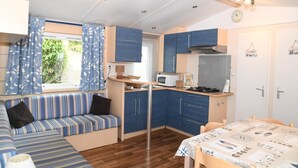 A compact kitchen with a dining area, a built-in bench, and a small table. - Camping Le Pré Fleuri (Le Crotoy)