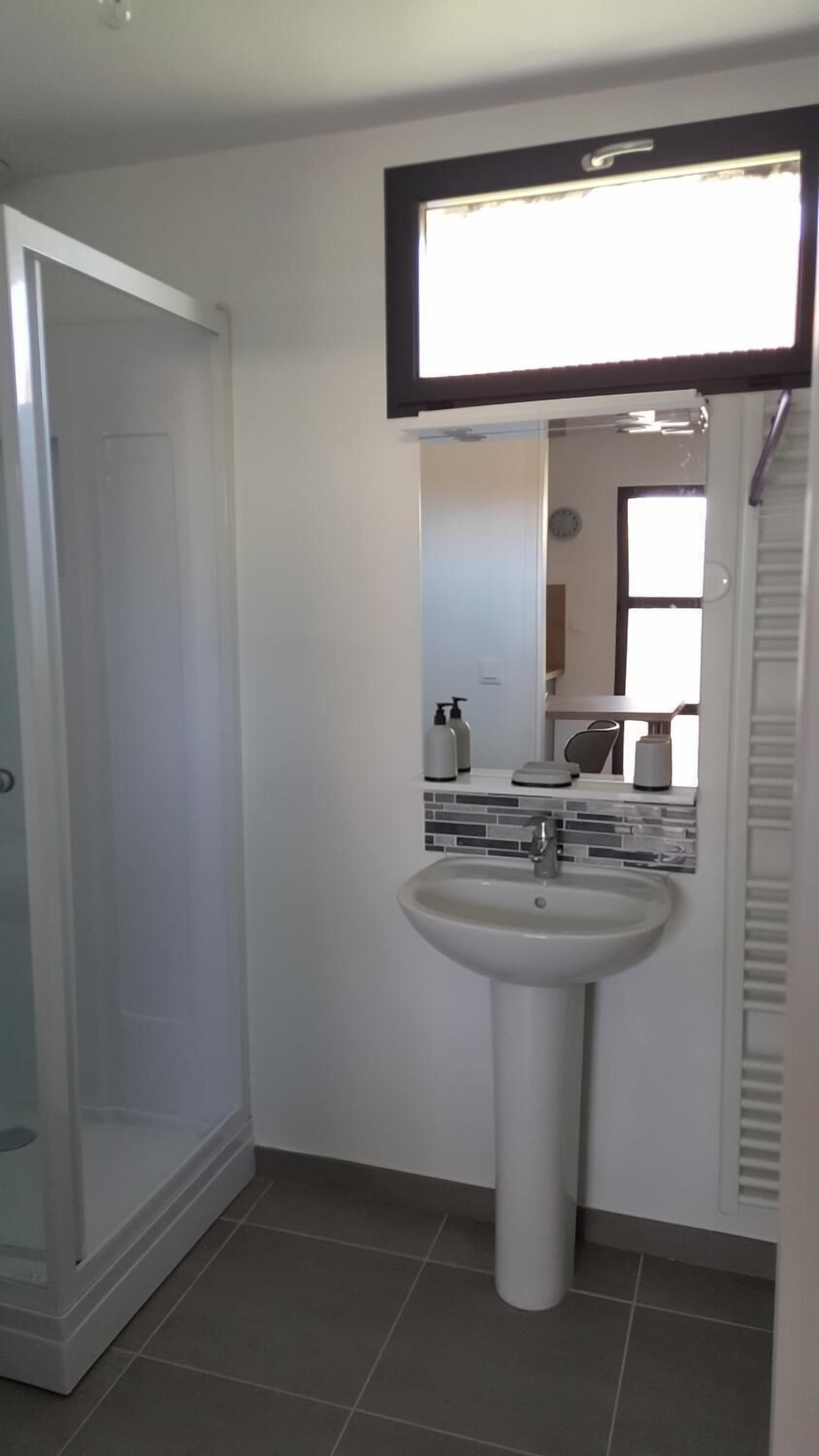 A bathroom with a pedestal sink, a mirror, and a shower enclosure.