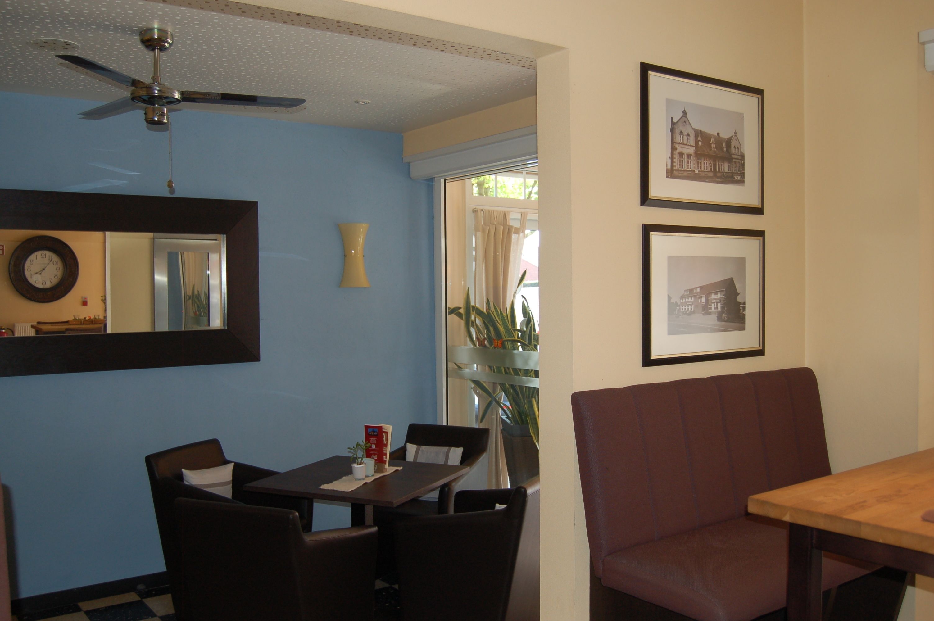 A dining area with a table, chairs, a ceiling fan, and framed pictures on the wall.