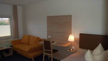 Una habitación de hotel con una cama, un escritorio, una silla, un sofá y una lámpara.