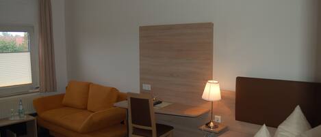 Ein Hotelzimmer mit Bett, Schreibtisch, Sessel, Sofa und Lampe.