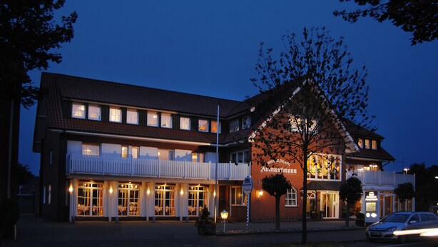 A hotel with a traditional European architectural style, featuring a prominent entrance with a sign, multiple windows, and a well-lit facade.