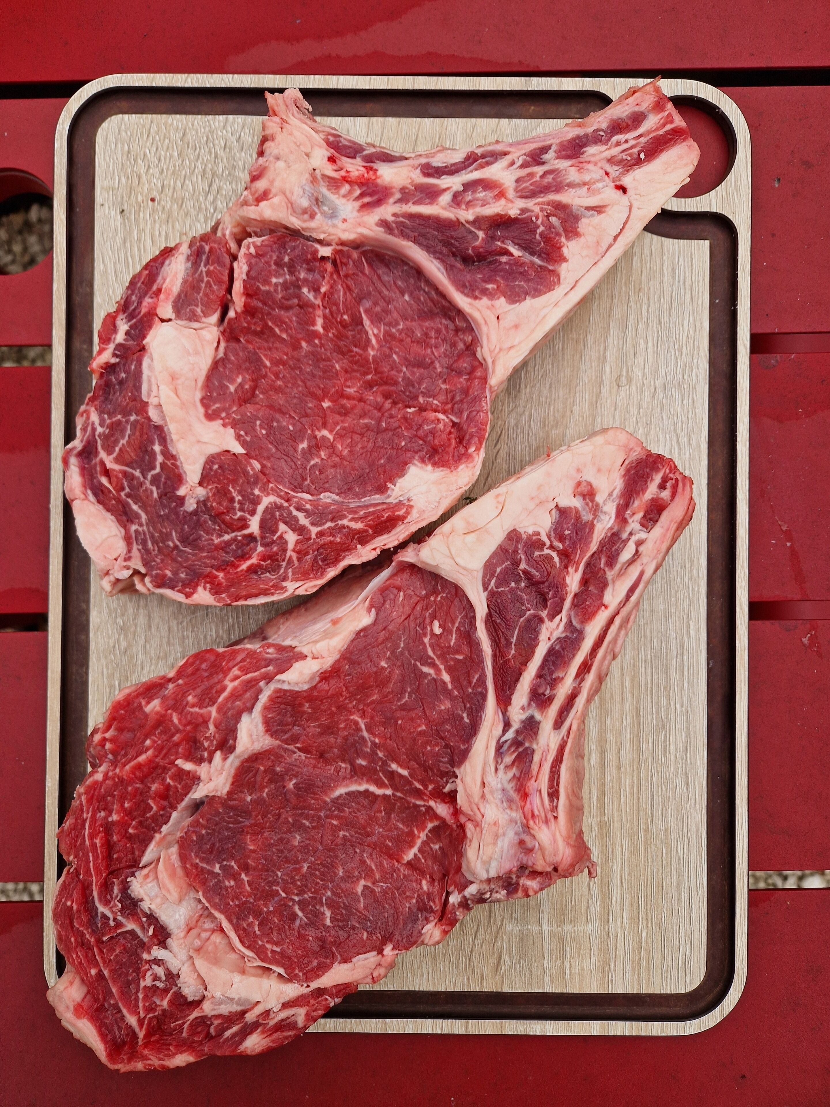 Deux steaks crus sur une planche à découper en bois.
