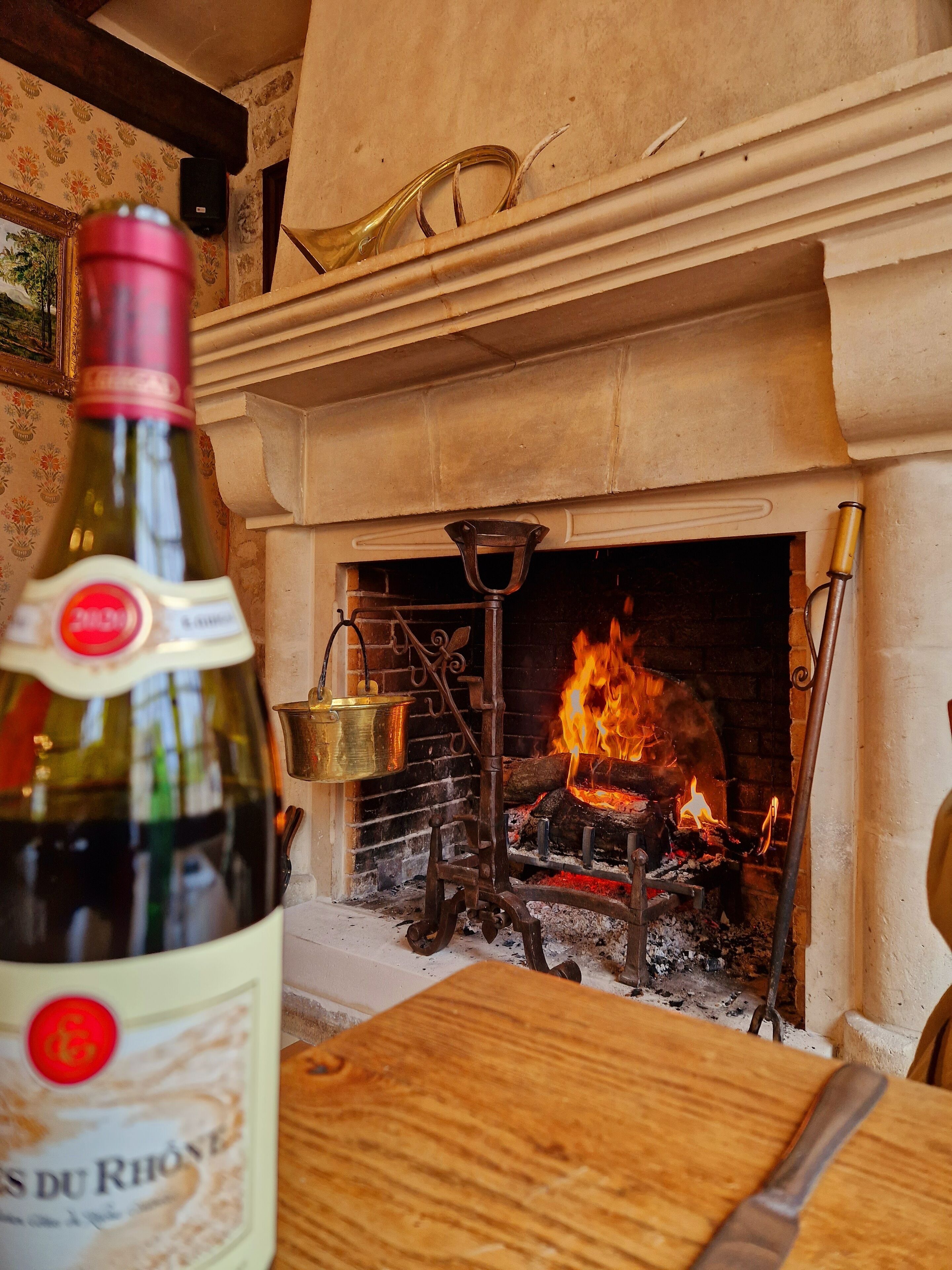 Una bottiglia di vino su un tavolo di legno, con un camino sullo sfondo.