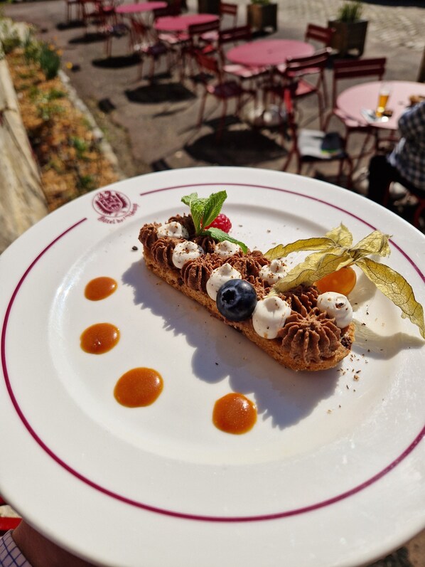 A dessert on a plate with a logo, surrounded by a table and chairs. - Hotel De L'Abbaye (Longpont)