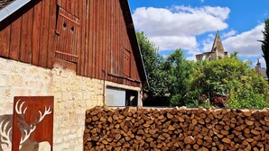 A rustic barn with a sloped roof, a wooden deer sculpture, and a stack of firewood. - Hotel De L'Abbaye (Longpont)