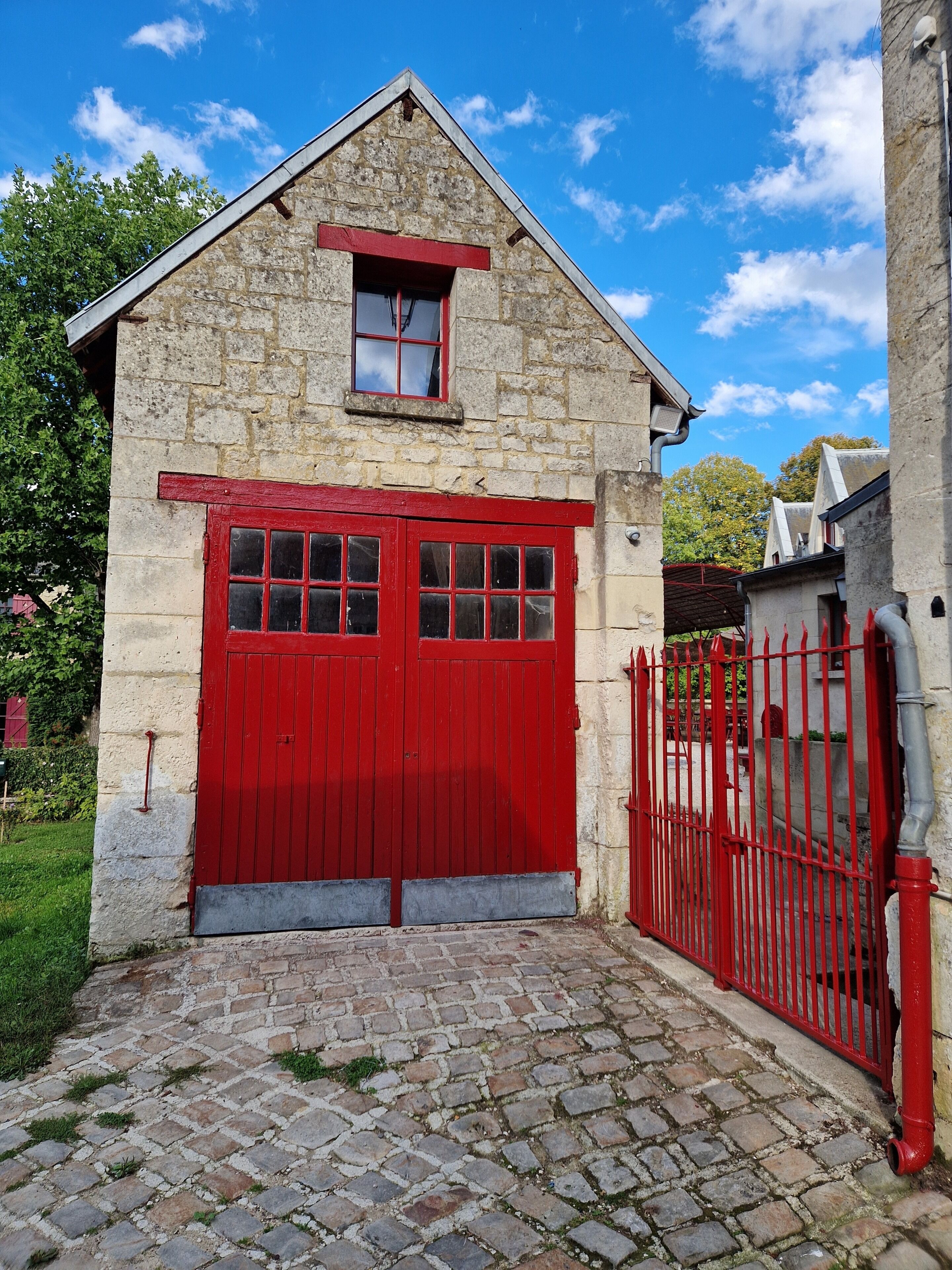 A stone building with a red door and window, a cobblestone path, and a red fence.