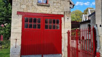 A stone building with a red door and window, a cobblestone path, and a red fence.