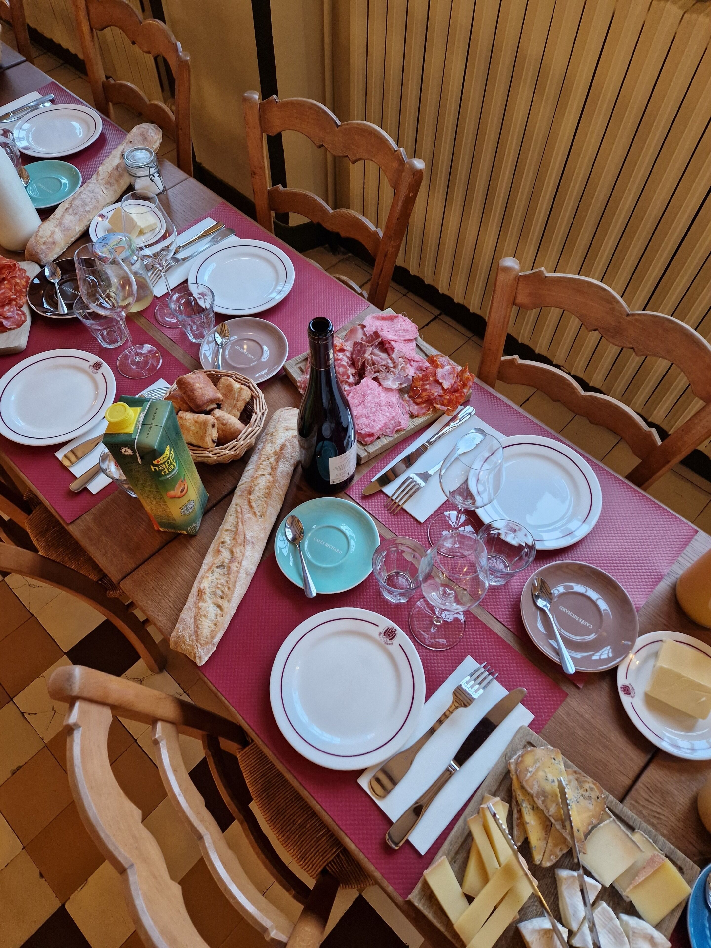 Una mesa de comedor dispuesta con platos, cubiertos, vasos, pan y una botella de vino.