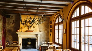 A dining area with wooden tables and chairs, a fireplace, and large arched windows. - Hotel De L'Abbaye (Longpont)