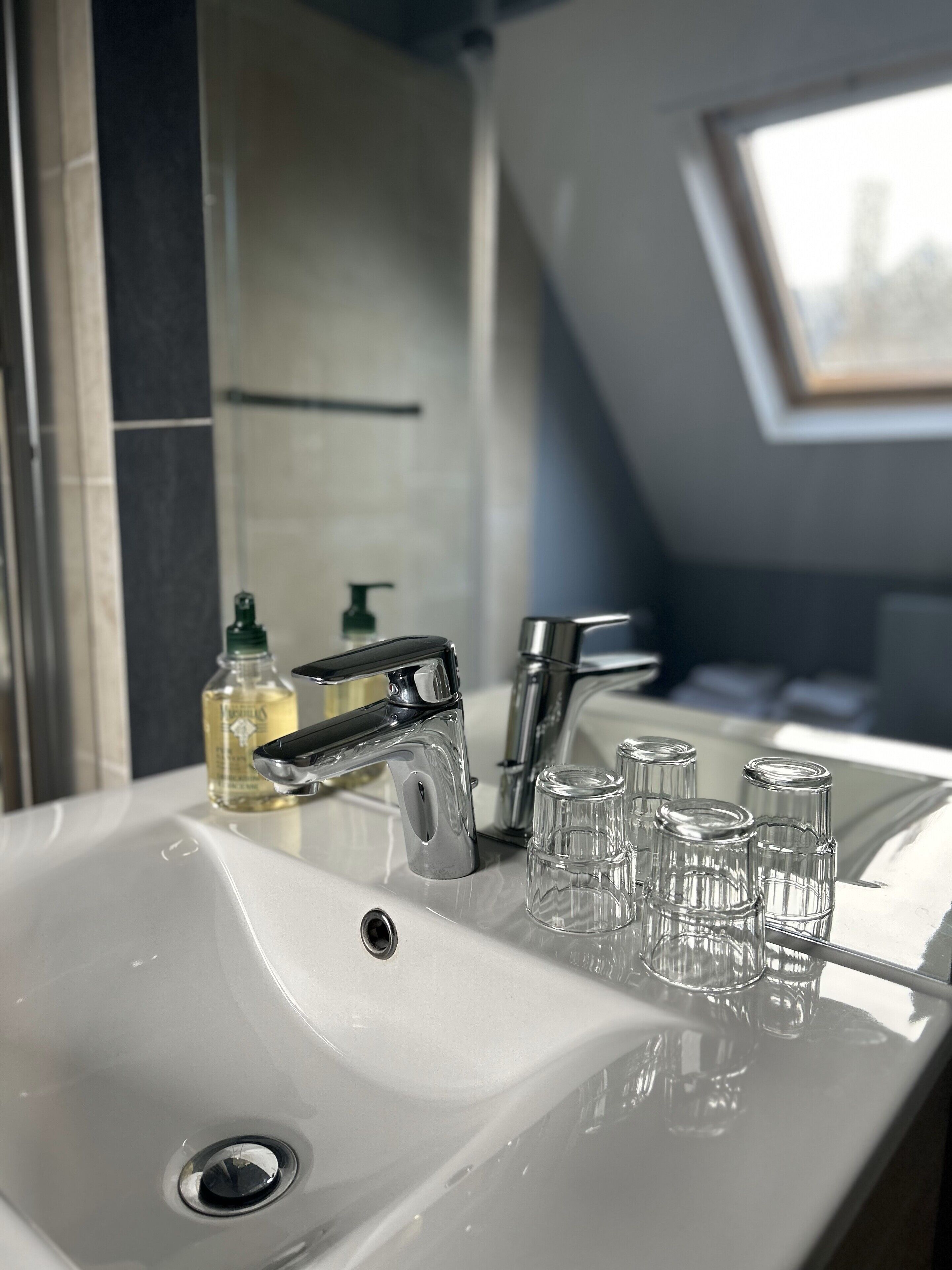 Een badkamer met een wit wastafelmeubel, twee kranen en drie glazen op het aanrecht.