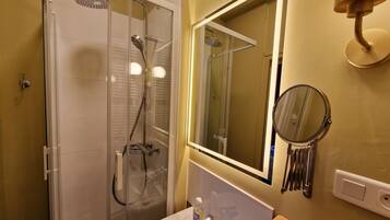 Een badkamer met een glazen douchecabine, een wastafel met spiegel en een houten krukje.