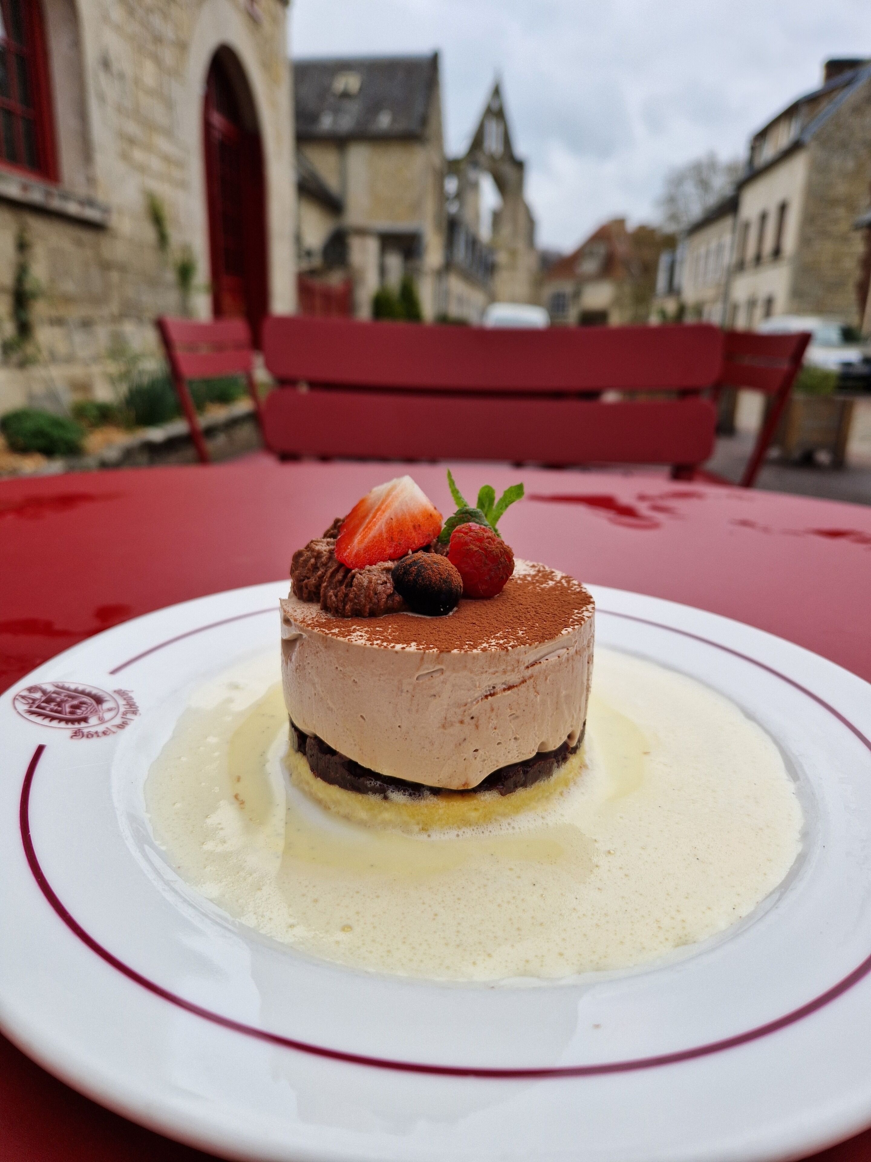 A dessert on a plate with a red tablecloth, set outdoors with a red bench and stone buildings in the background.