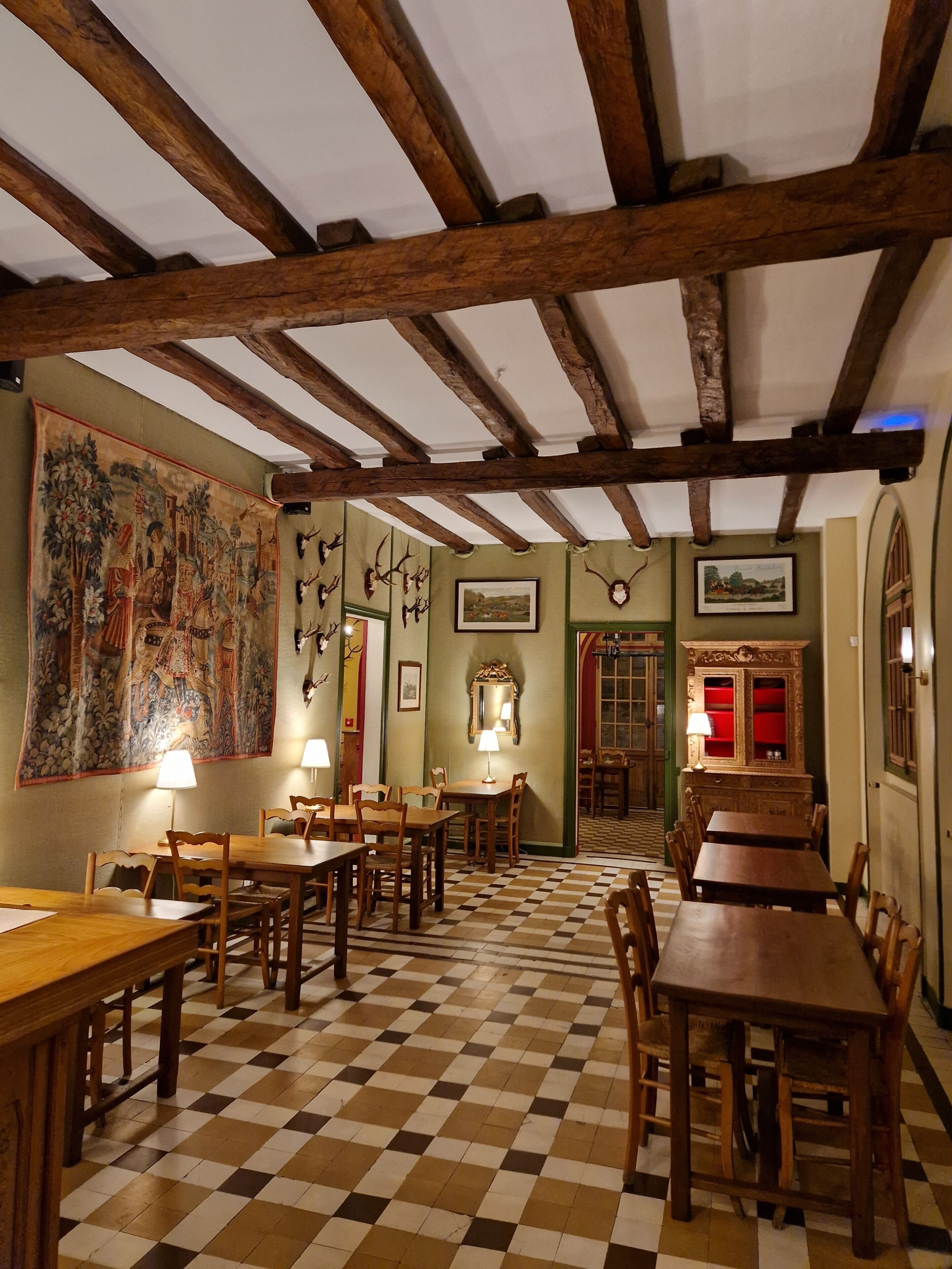 A room with wooden beams, checkered floor, tables, chairs, and wall-mounted decorations.