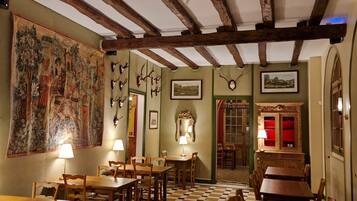 A room with wooden beams, checkered floor, tables, chairs, and wall-mounted decorations.
