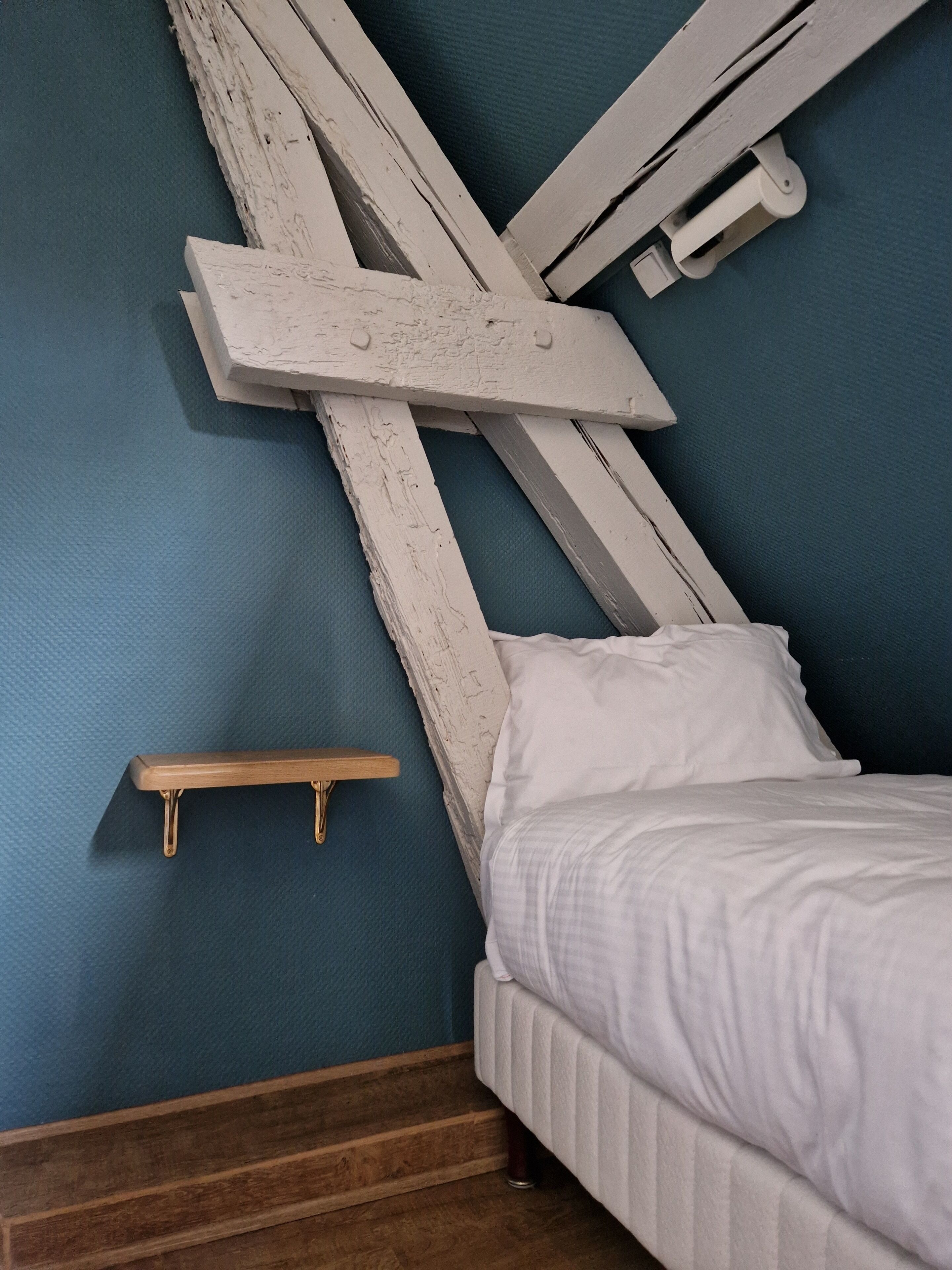 Une chambre à coucher avec un lit, une table de chevet en bois et une étagère fixée au mur.