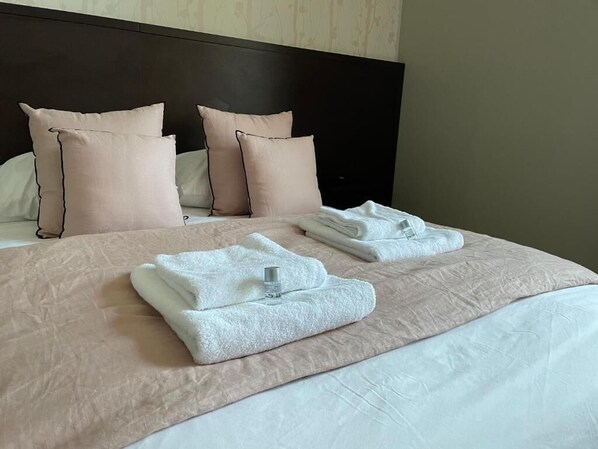Una cama bien hecha con ropa de cama rosa y almohadas, una toalla blanca doblada y una botella de loción sobre la cama.