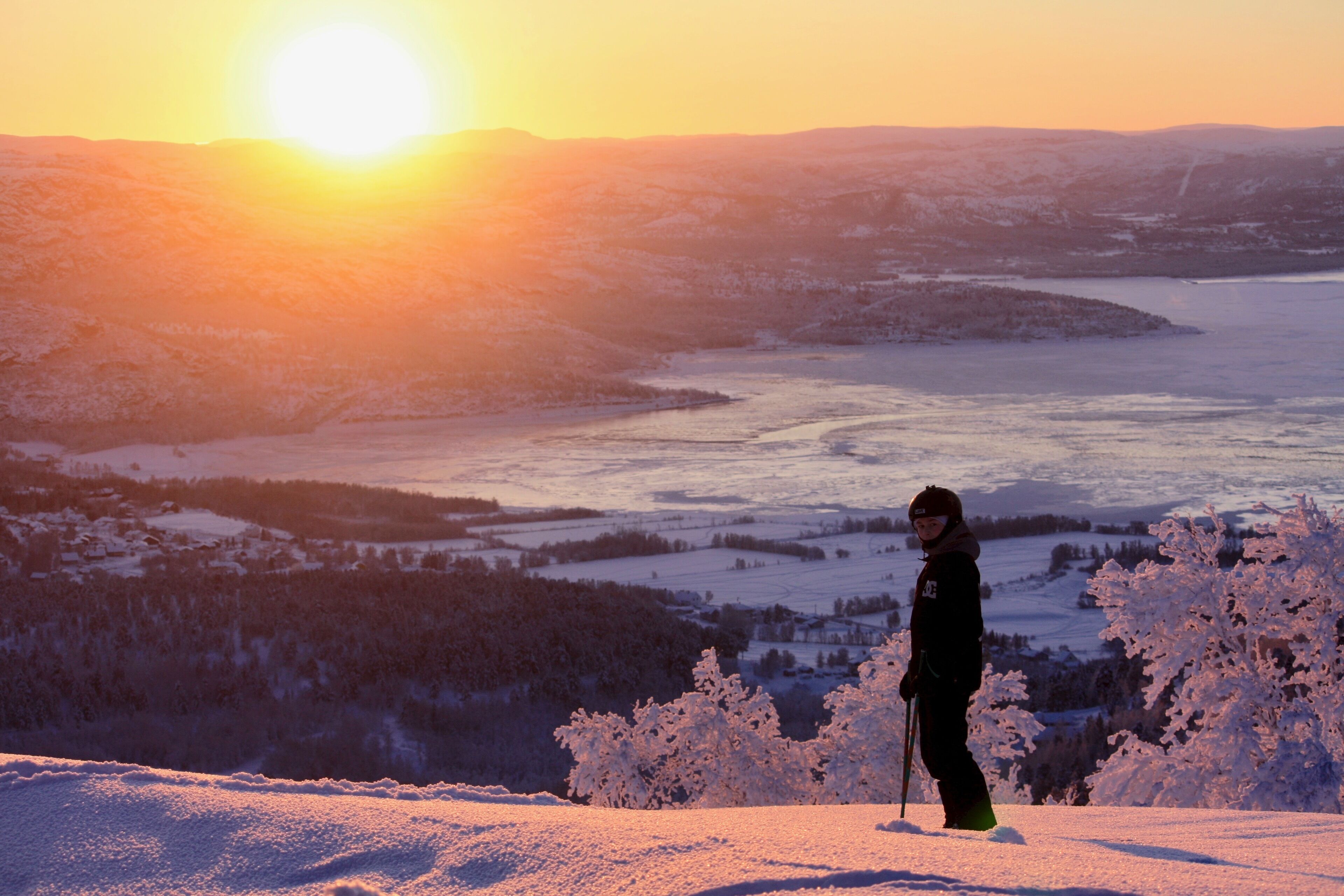 A person skiing on a snowy slope with a sunset in the background.
