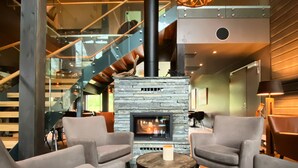 A modern interior with a stone fireplace, comfortable seating, and a staircase. - Bjørnfjell Mountain Lodge (Alta)