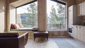 A modern kitchen with wooden cabinets, a built-in oven, and a large window overlooking a forest. - Bjørnfjell Mountain Lodge (Alta)