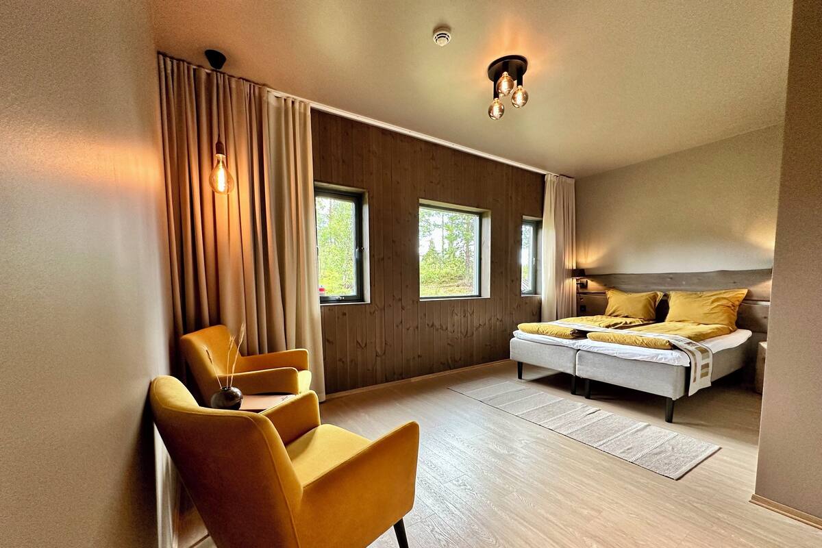 A modern bedroom with a bed, a chair, and large windows.