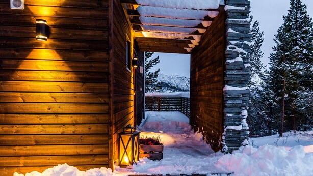 A wooden cabin with a snow-covered entrance and a stone wall. - Bjørnfjell Mountain Lodge (Alta)
