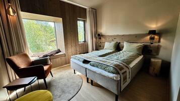 A bedroom with a bed, a chair, a small table, a lamp, and a window with curtains.