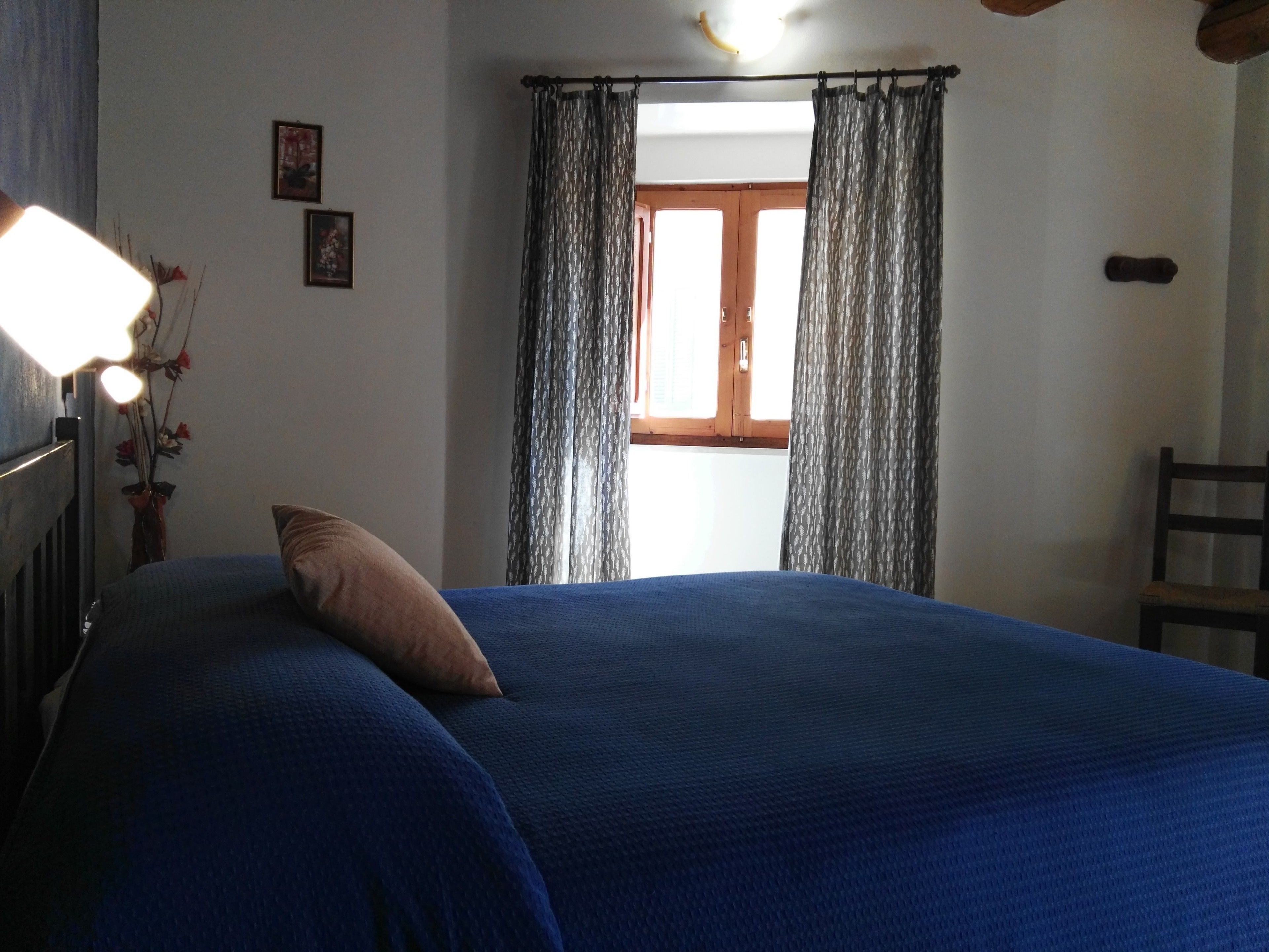 A bedroom with a bed, a nightstand, a lamp, a chair, and a window with curtains.