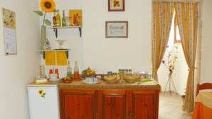 A compact kitchen with wooden cabinets, a refrigerator, and a small countertop. There are various kitchen items and decorations on the shelves and counter. - Cloris Guest House (Noto)