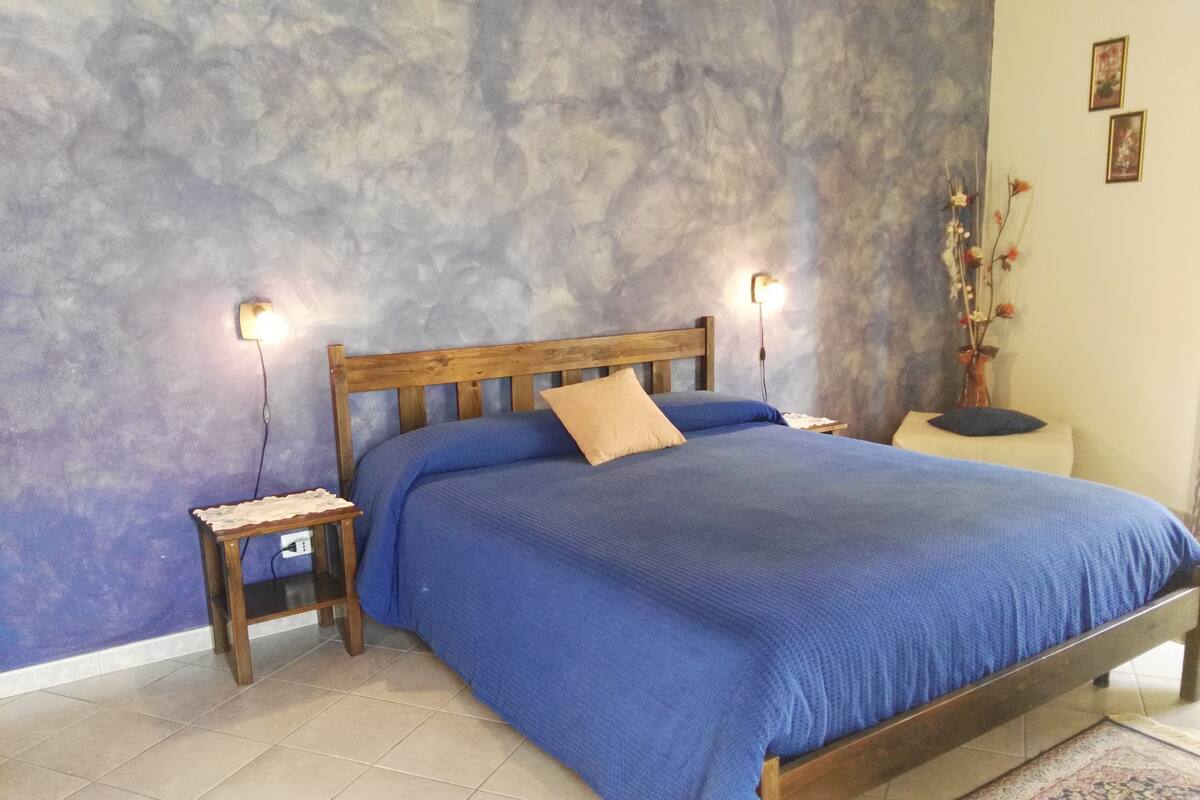 A bedroom with a wooden bed, two bedside tables, a nightstand, a vase with flowers, and a textured wall.