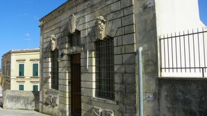 A stone building with a wooden door and barred windows. - Cloris Guest House (Noto)