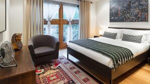 Une chambre moderne avec un grand lit, une vue sur la ville, un ventilateur, une chaise et un élément décoratif au niveau de la tête de lit.