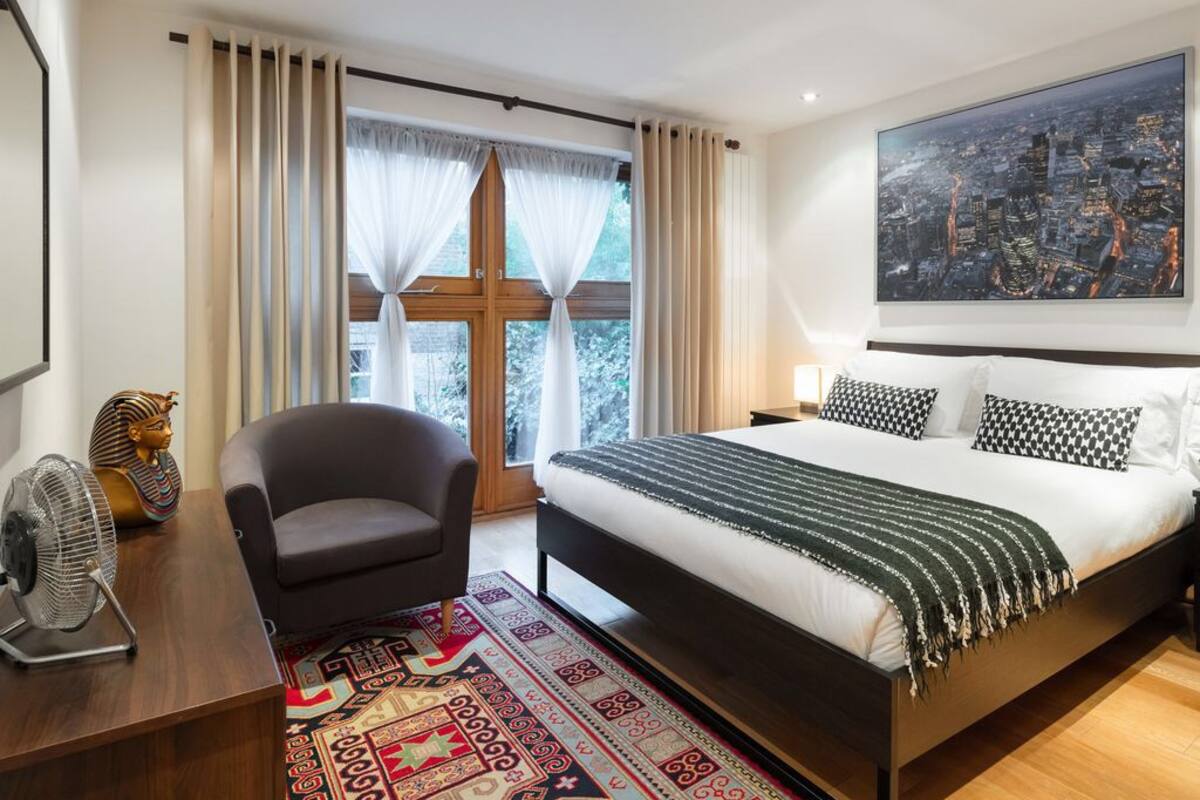 Un dormitorio moderno con una cama grande, vistas a la ciudad, un ventilador, una silla y un adorno en la cabecera.