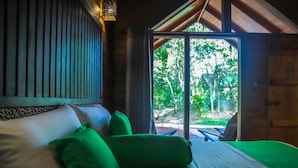 A wooden room with a bed, green pillows, and a view of the outdoors.