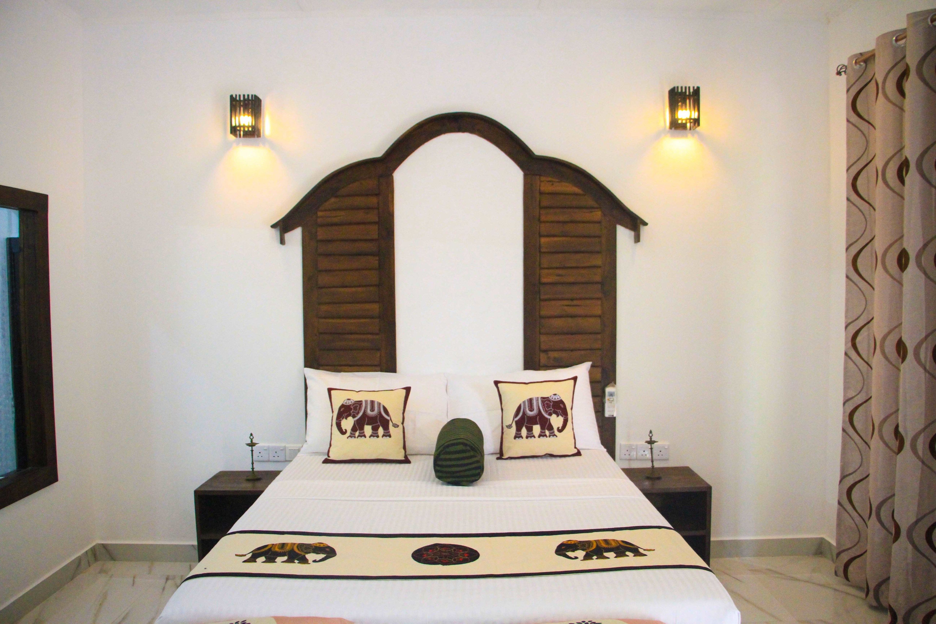 Quarto com cama, duas mesas de cabeceira, duas luminárias fixadas na parede, cabeceira decorativa e cortinas estampadas.