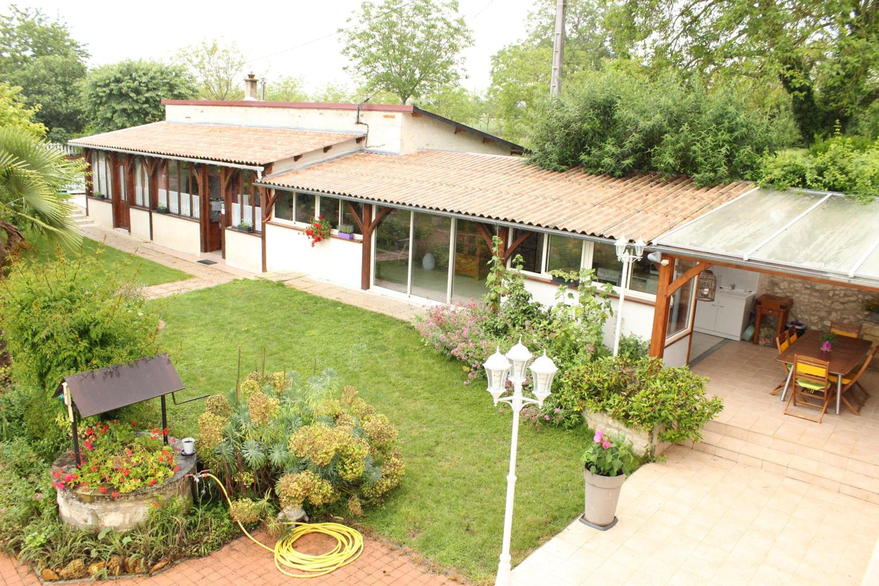Ein Haus mit überdachter Terrasse, einem Garten mit verschiedenen Pflanzen und einer Solaranlage.