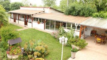 Ein Haus mit überdachter Terrasse, einem Garten mit verschiedenen Pflanzen und einer Solaranlage.