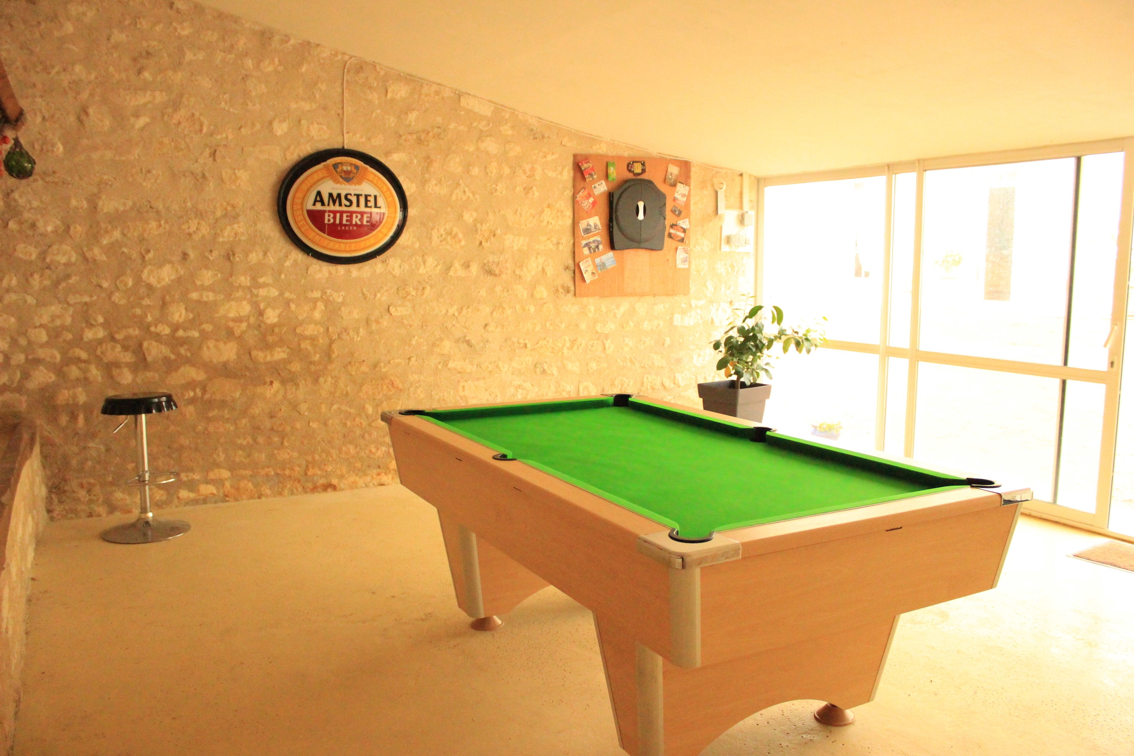 Una mesa de billar en una habitación con pared de piedra, un letrero de cerveza enmarcado y una ventana con vistas.