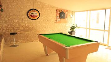 Una mesa de billar en una habitación con pared de piedra, un letrero de cerveza enmarcado y una ventana con vistas.