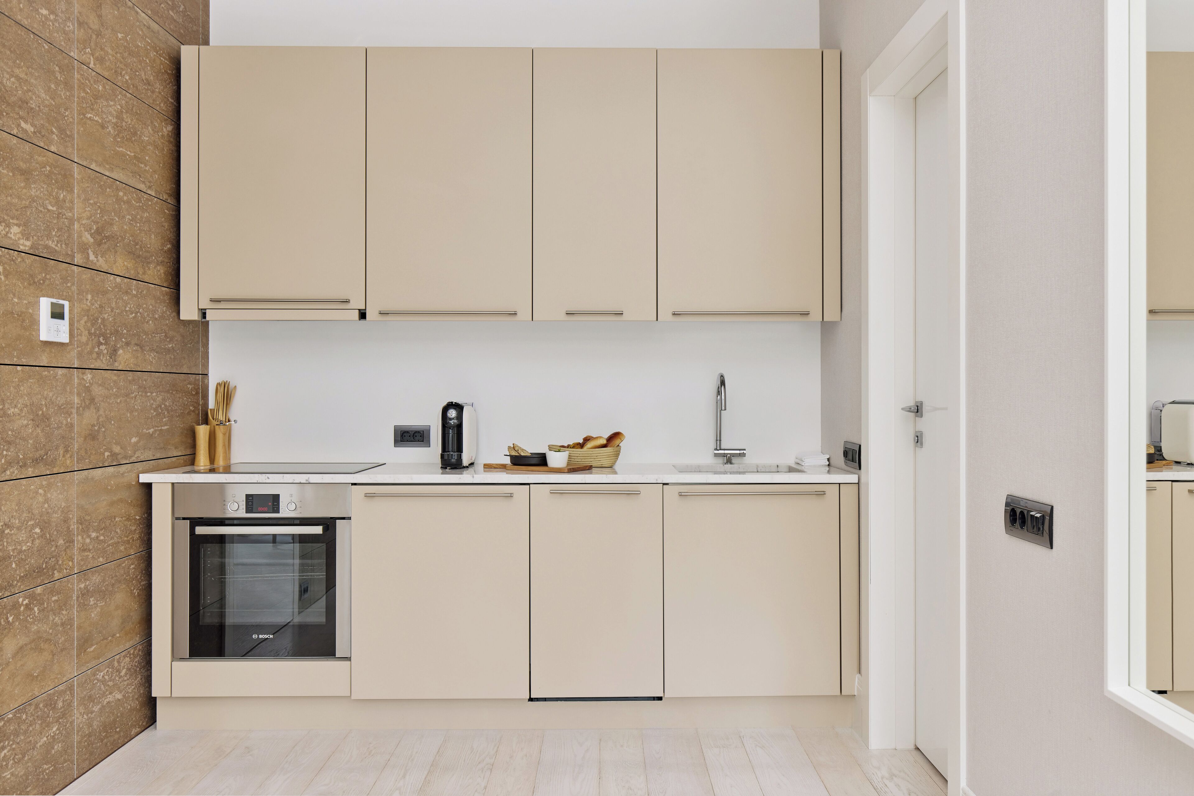 A modern kitchen with beige cabinetry, a built-in oven, and a countertop with a coffee maker and bread basket.
