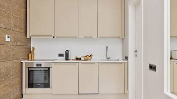 A modern kitchen with beige cabinetry, a built-in oven, and a countertop with a coffee maker and bread basket.