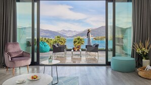 A modern living room with a large sliding glass door leading to a balcony with a scenic mountain and lake view. - Monte Palm Beach (Durasevici)