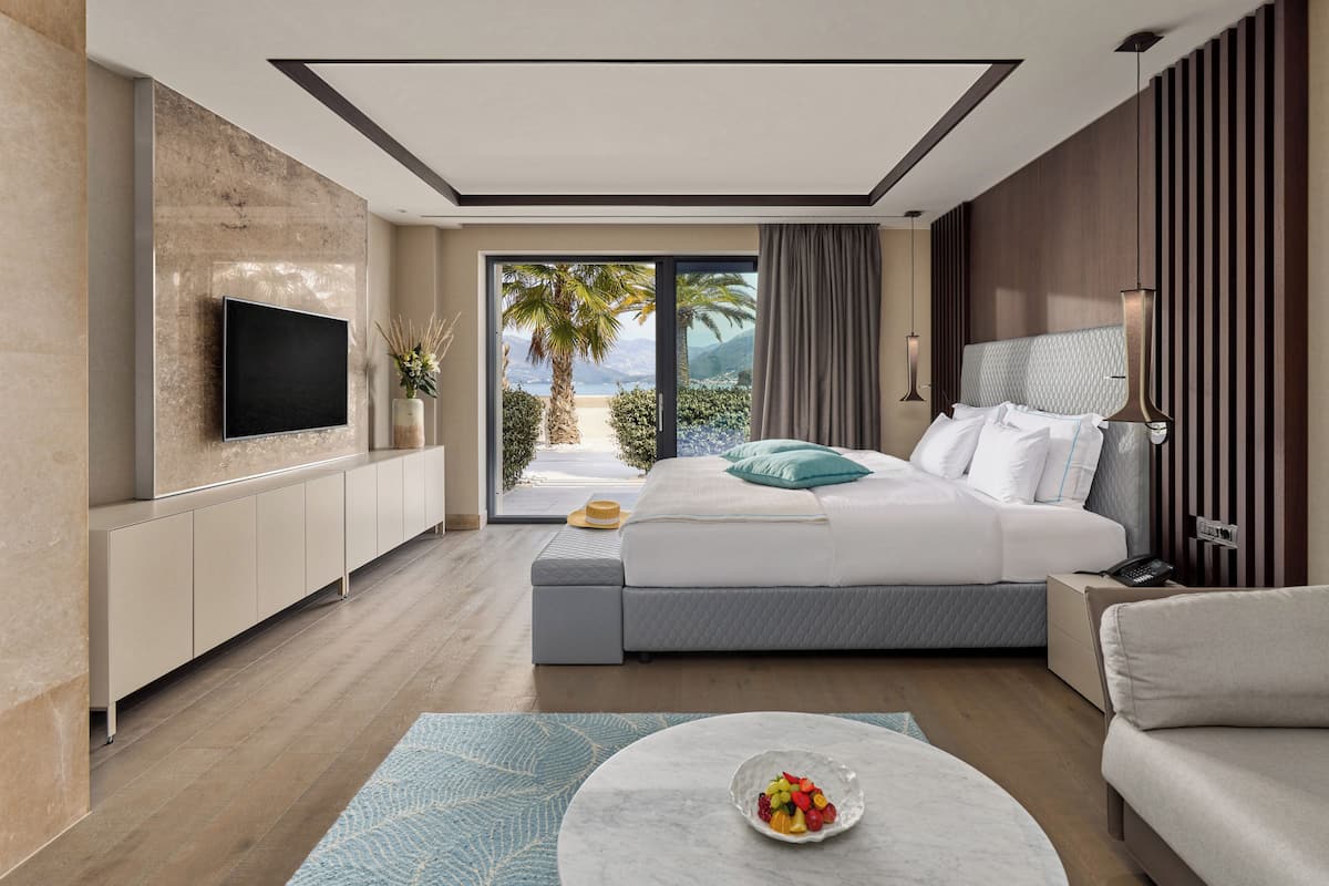 A modern bedroom with a bed, a TV, a bedside table, and a view of the outdoors.