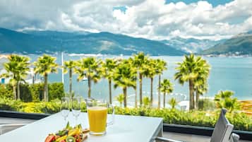 Enjoy a meal with a view of the coastal landscape from this dining area, featuring a table set for two and a scenic view of palm trees and a body of water.