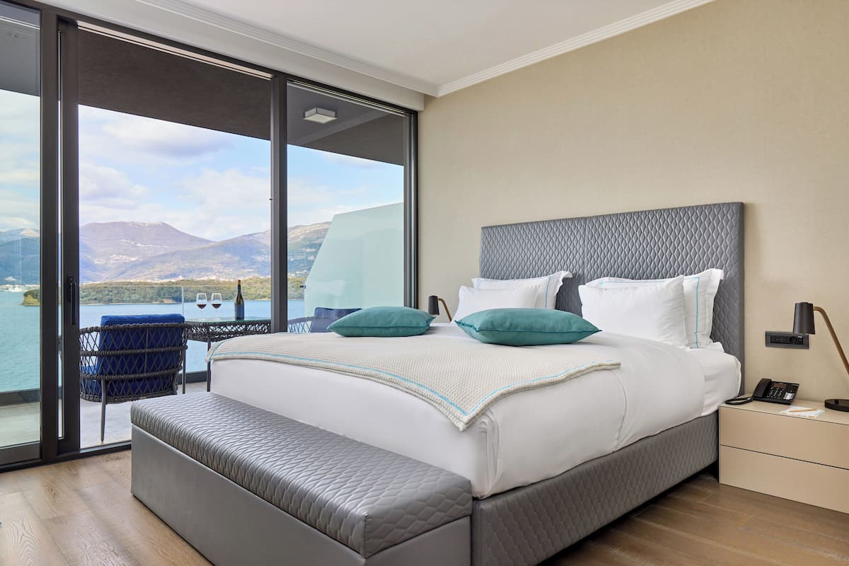 A modern hotel room with a large bed, a bench, a nightstand, and a view of the sea.