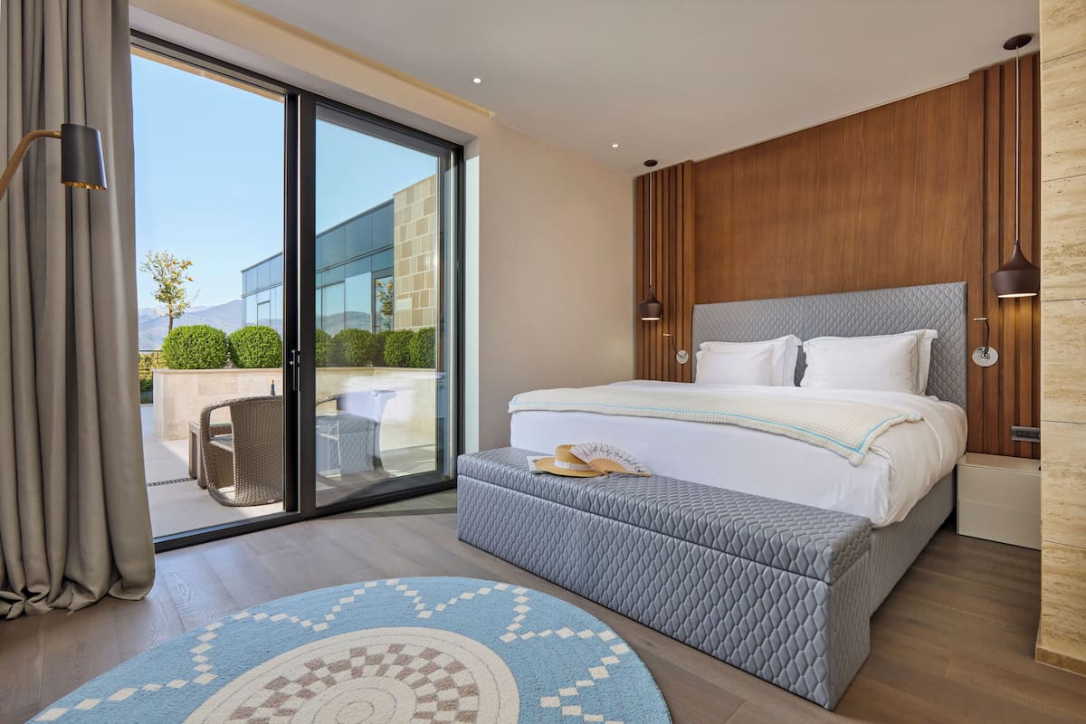 A modern bedroom with a large bed, a sliding glass door to a patio, and a small seating area.