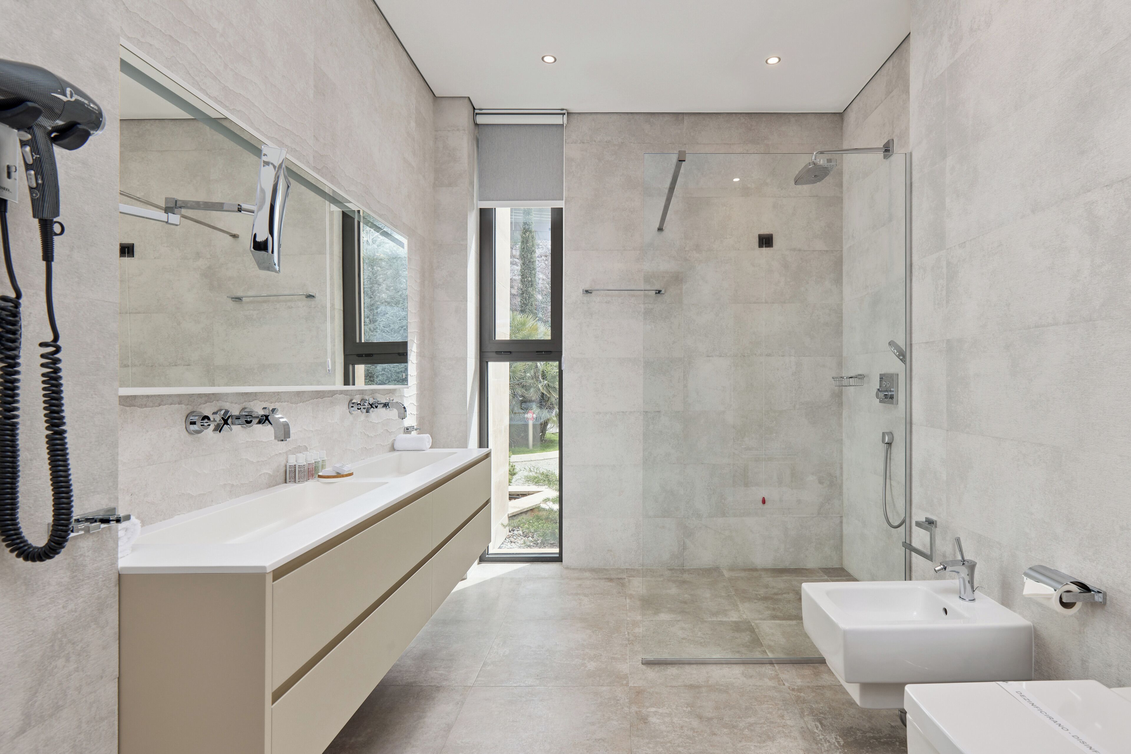 Une salle de bain moderne dotée d’un grand miroir, de deux lavabos, d’une douche et d’un sèche-cheveux.